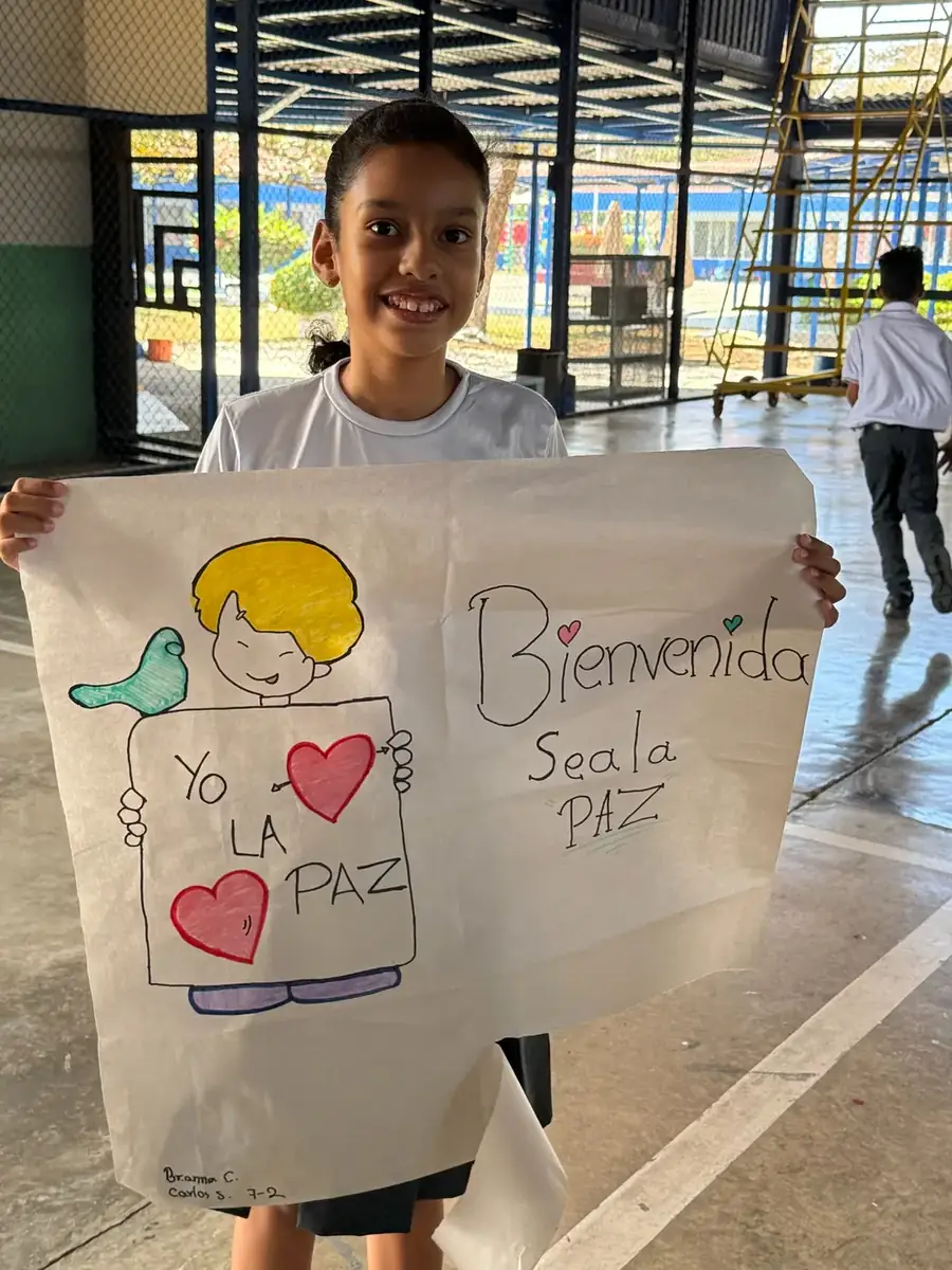 Smiling child holding a handmade welcome poster with peace messages during Choral Fest Costa Rica for Peace.
